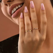 Close-up of a hand with pink nail polish and 14k gold filled diamonds rings, against a neutral background